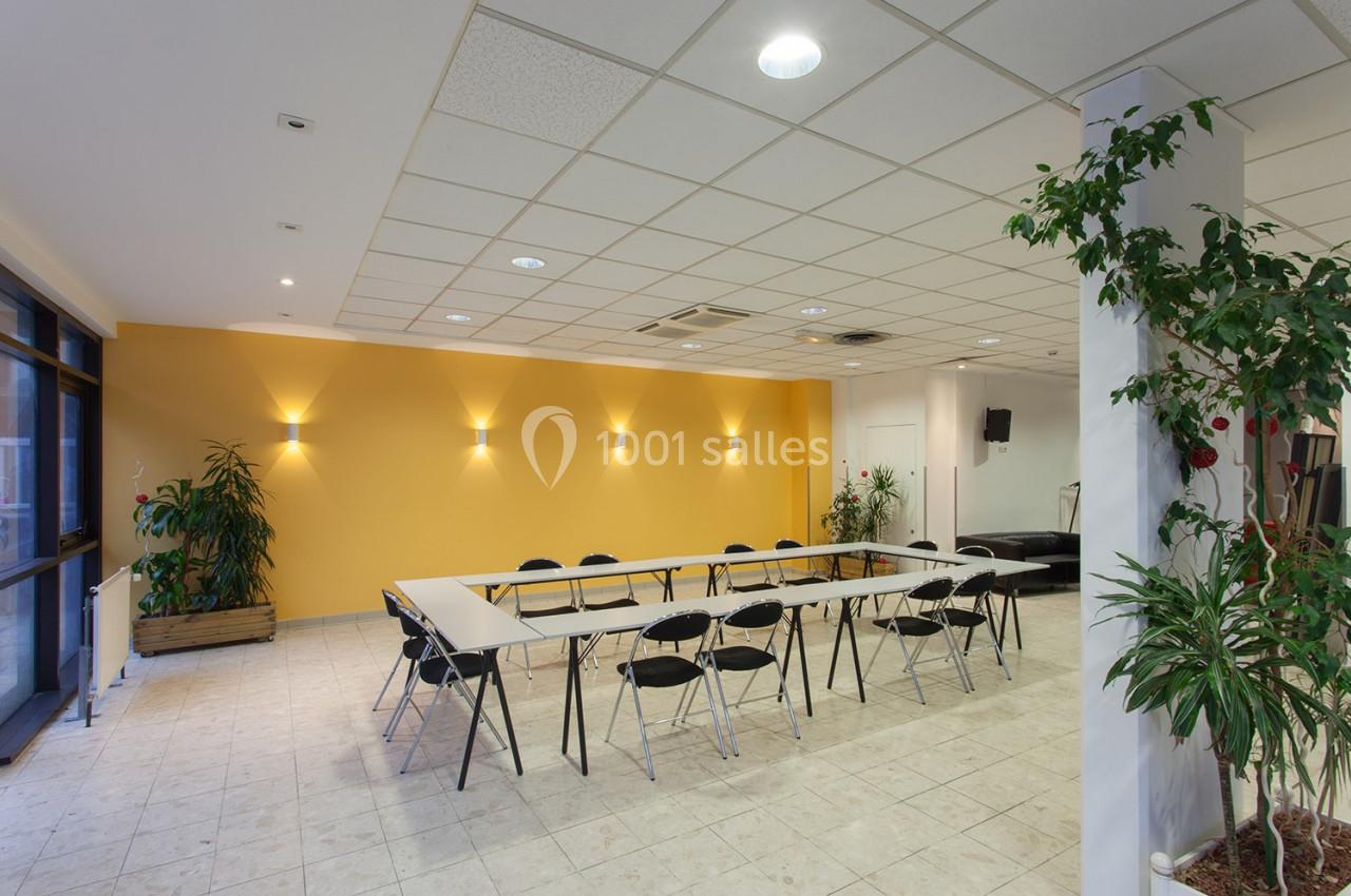 Salle de réunion lumineuse avec murs jaunes, tables disposées en U, chaises noires et plantes en décoration.