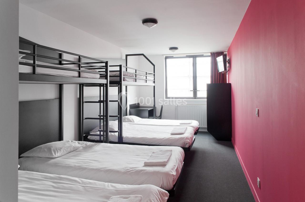 Chambre avec lits superposés et simples, murs blancs et rouges, fenêtre lumineuse et mobilier minimaliste.