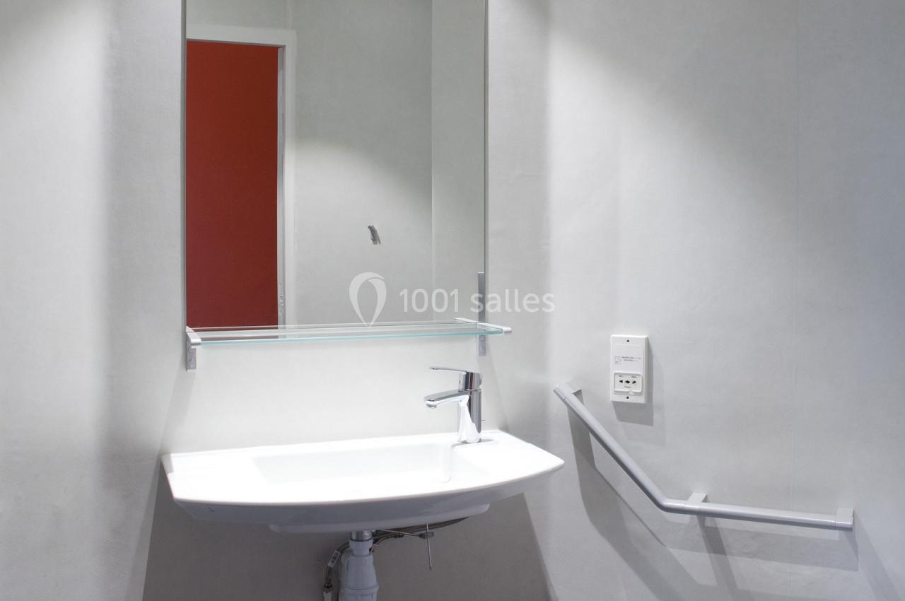 Salle de bain accessible avec lavabo suspendu, miroir, barre d'appui et toilettes adaptées.