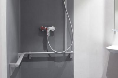 Douche accessible avec barre d'appui, siège rabattable et pommeau de douche réglable.