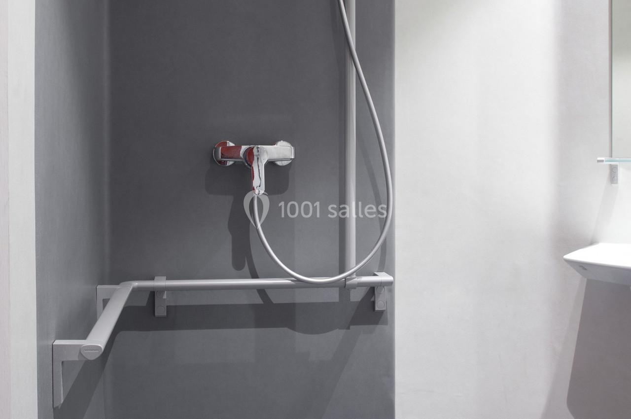 Douche accessible avec barre d'appui, siège rabattable et pommeau de douche réglable.