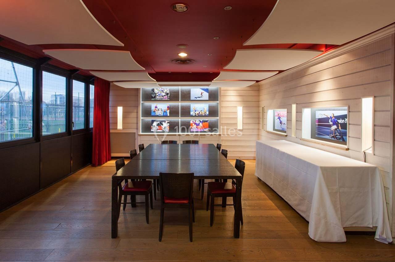Salle de réunion moderne avec table en bois, chaises, éclairage mural et photos sportives exposées.