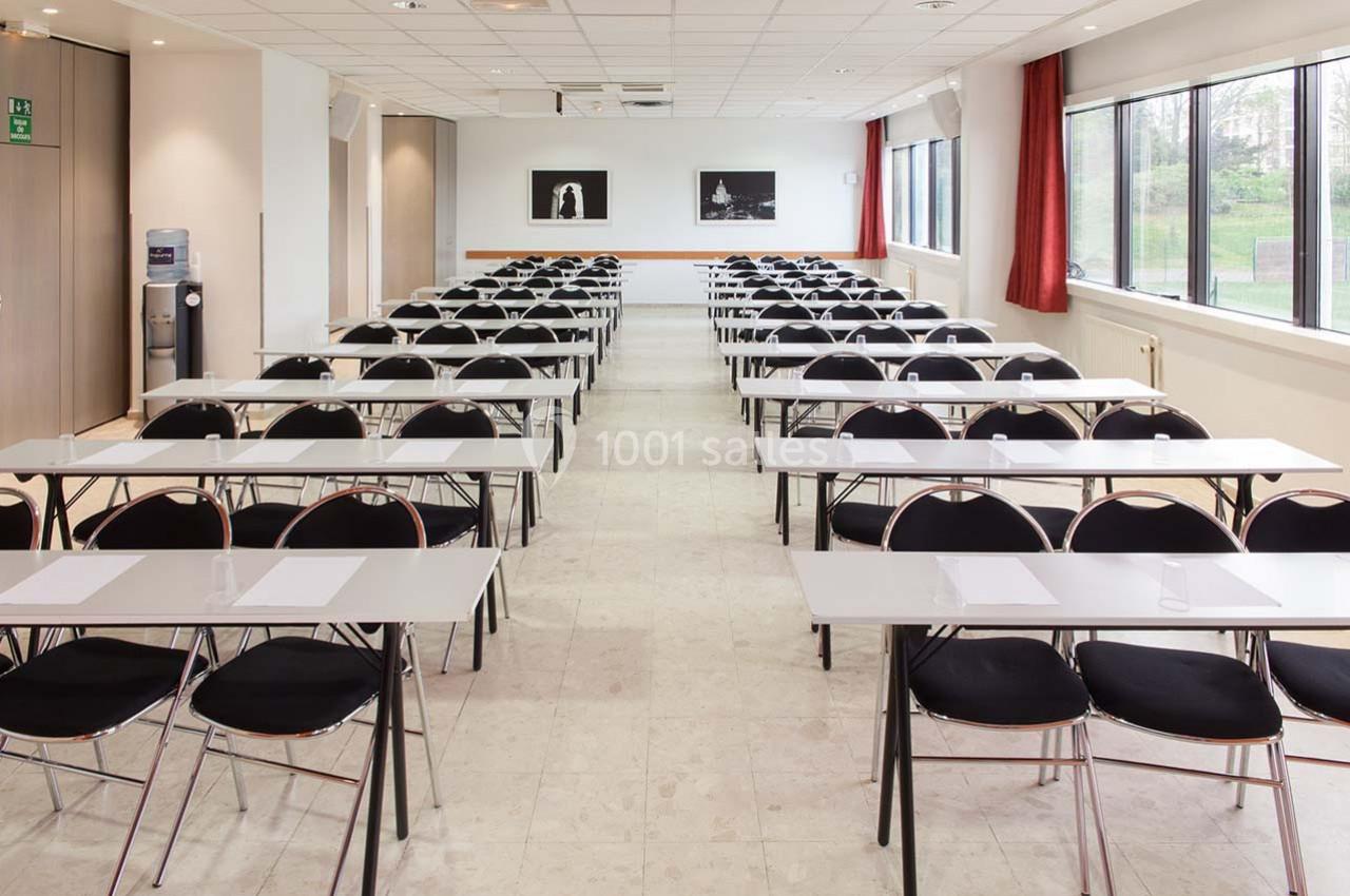 Salle de conférence lumineuse avec des rangées de tables et chaises alignées, prête pour une réunion ou un séminaire.