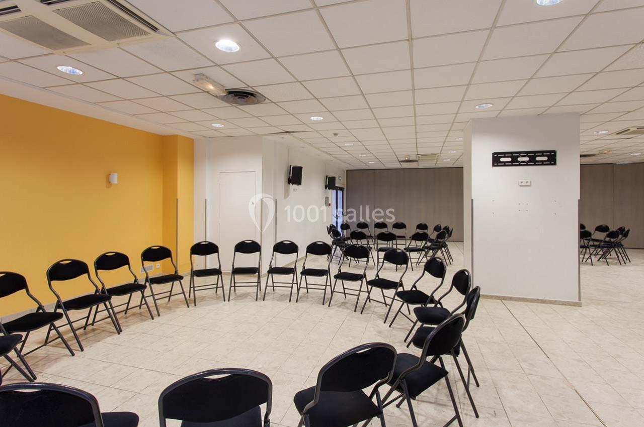 Salle de réunion avec des chaises noires disposées en cercle sur un sol carrelé, murs blancs et jaunes.