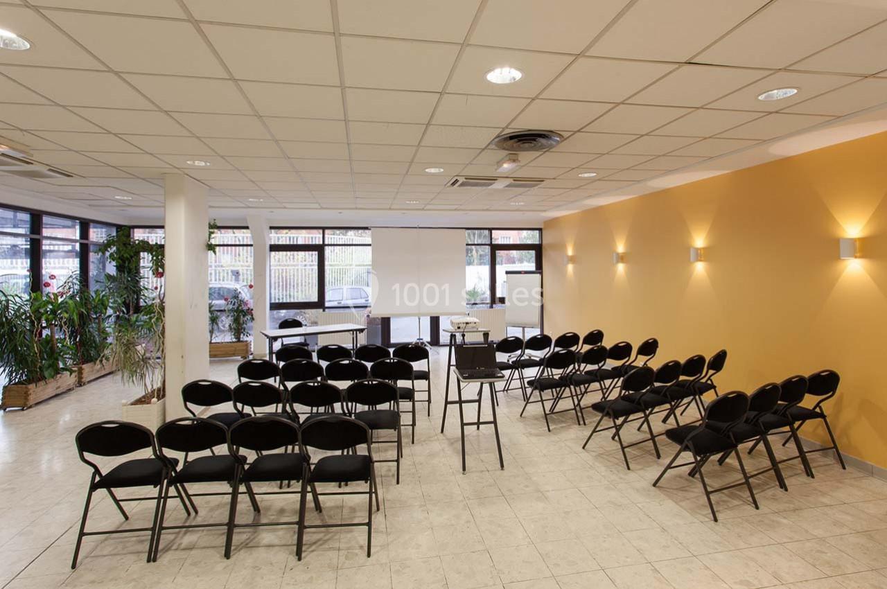 Salle de réunion lumineuse avec des chaises disposées face à un écran de projection et un tableau blanc.