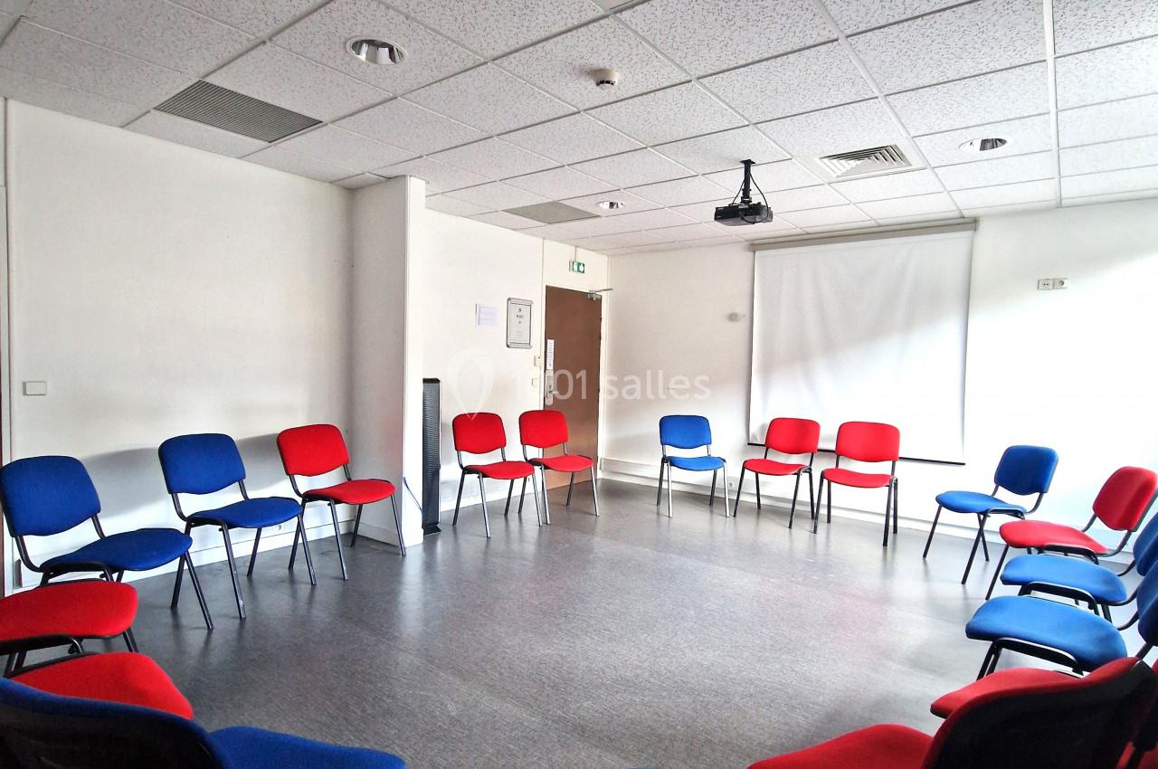 Salle de réunion avec des chaises rouges et bleues disposées en cercle, éclairée par une lumière naturelle.