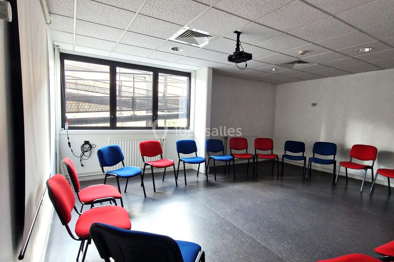 Salle de réunion lumineuse avec des chaises rouges et bleues disposées en cercle sur un sol sombre.