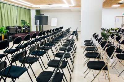 Chambre lumineuse avec deux lits simples, une table, une lampe, une fenêtre avec rideaux et une étagère grise.