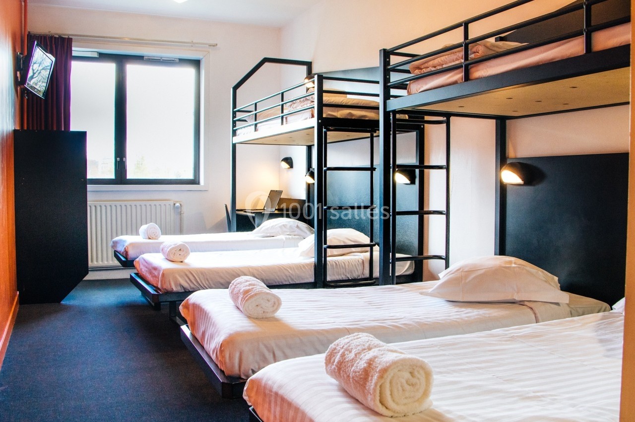 Chambre avec lits superposés et lits simples, éclairage mural, fenêtre lumineuse et télévision fixée au mur.