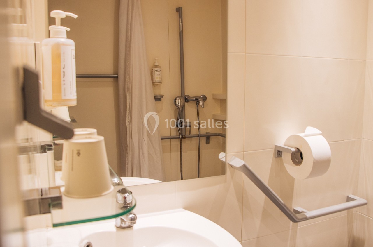 Salle de bain accessible avec barre d'appui, douche équipée et lavabo avec accessoires.