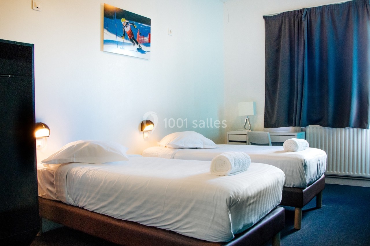 Deux lits simples avec draps blancs dans une chambre lumineuse, décorée d'un tableau et équipée d'un bureau.