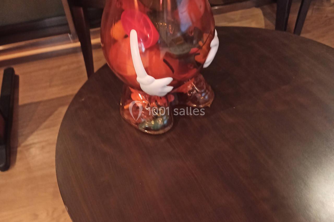 Figurine en plastique translucide en forme de patate, portant un chapeau beige, posée sur une table en bois.