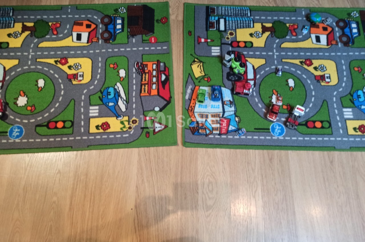 Deux tapis pour enfants avec des motifs de routes, véhicules et bâtiments, posés sur un sol en bois clair.