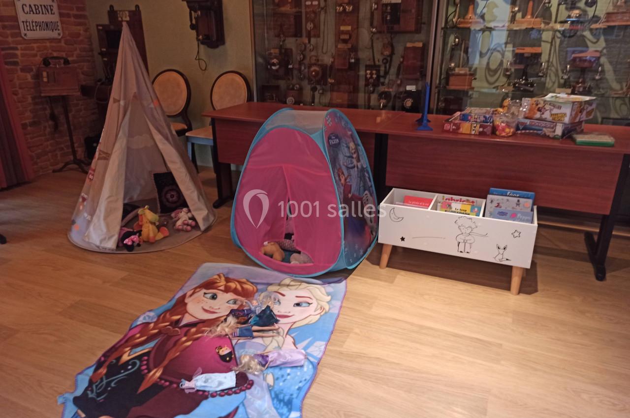 Espace de jeu pour enfants avec tentes, jouets, tapis décoré et meubles en bois dans une pièce au style rétro.