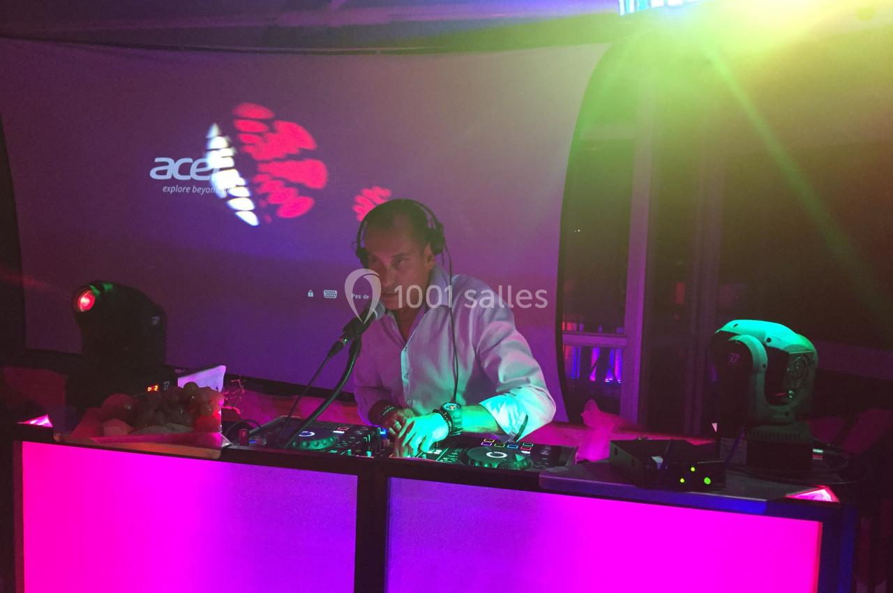 Un DJ mixant de la musique sur une table de mixage éclairée par des lumières colorées dans une ambiance nocturne.