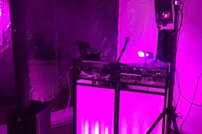 Table de mixage avec platines, microphones et panneau lumineux indiquant ’DJ Olivier’ sur une table en bois.