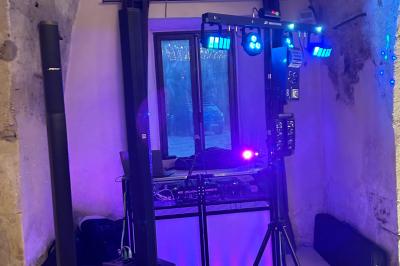 Table de mixage avec platines, microphones et panneau lumineux indiquant ’DJ Olivier’ sur une table en bois.