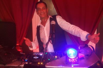 Table de mixage avec platines, microphones et panneau lumineux indiquant ’DJ Olivier’ sur une table en bois.