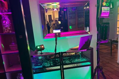 Table de mixage avec platines, microphones et panneau lumineux indiquant ’DJ Olivier’ sur une table en bois.