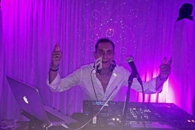 Un DJ souriant mixe de la musique sur une table de mixage, éclairé par une lumière violette dans une ambiance festive.