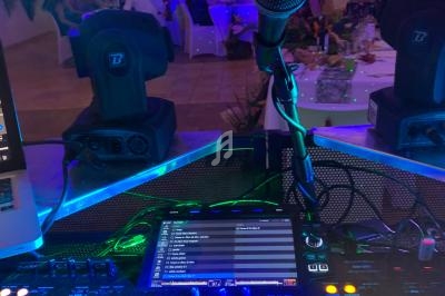 Vue depuis une table de mixage avec éclairage coloré, un micro au premier plan et des invités en arrière-plan.