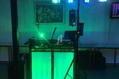Équipement de DJ avec éclairage LED vert, micros et haut-parleurs dans une salle sombre.