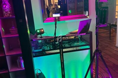 Poste de DJ avec éclairage coloré, ballons au sol et miroir reflétant une scène festive en arrière-plan.