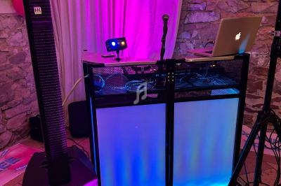 Poste de DJ avec éclairage coloré, enceintes, ordinateur portable et ballons décoratifs dans une salle en pierre.