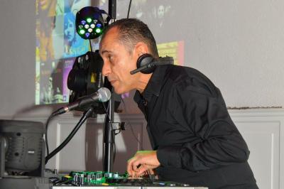 Table de mixage avec platines, microphones et panneau lumineux indiquant ’DJ Olivier’ sur une table en bois.