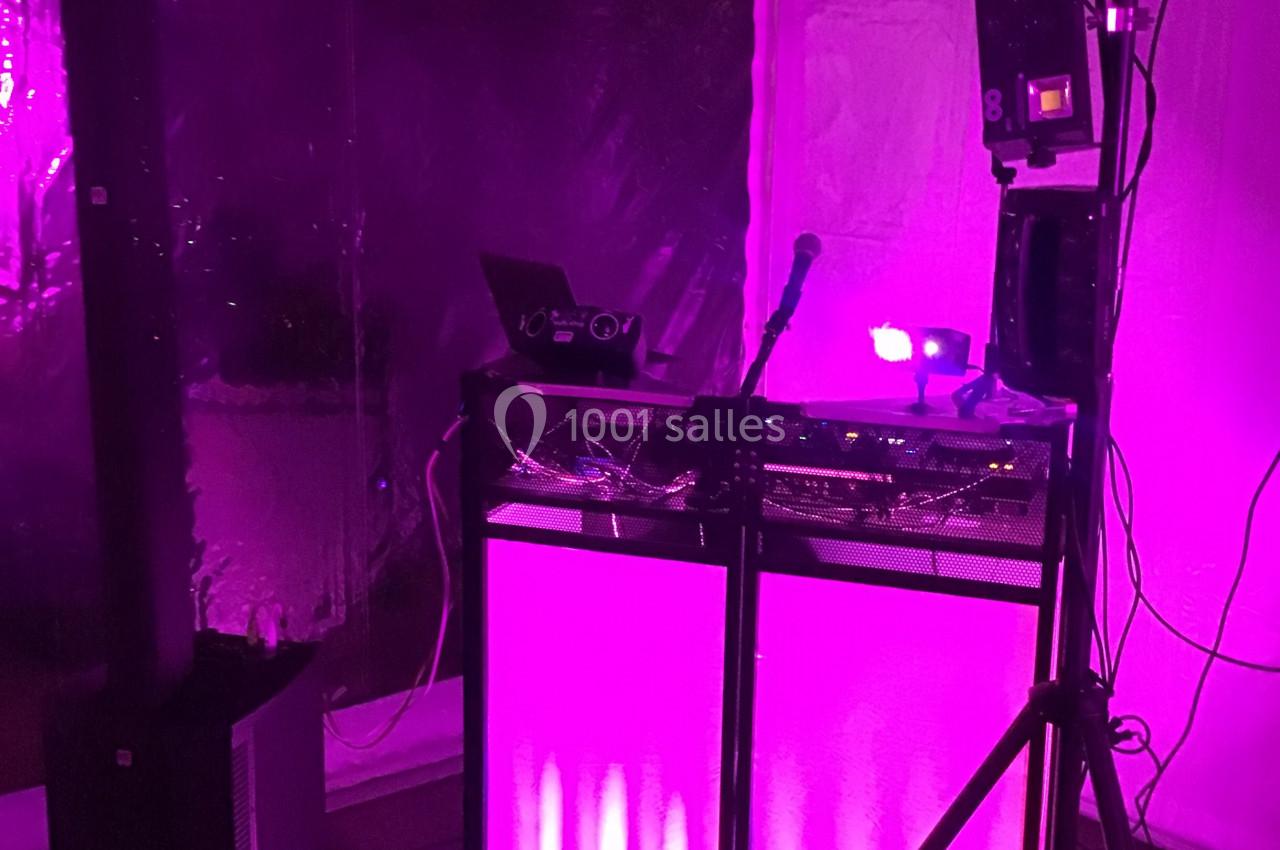 Poste de DJ éclairé par une lumière rose, avec un micro, un ordinateur portable et du matériel audio.