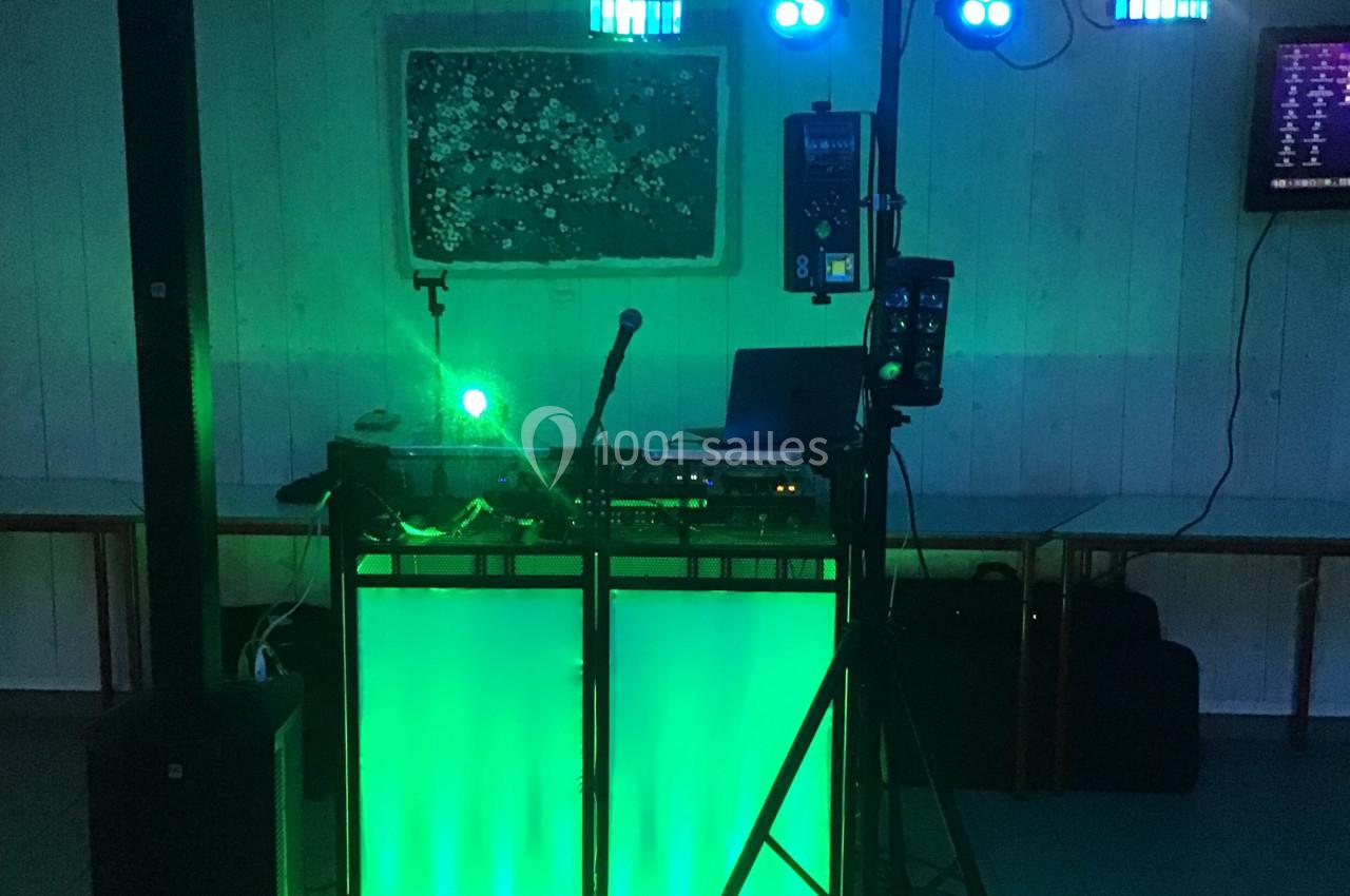 Table de mixage éclairée en vert avec micro, ordinateur et équipements audio dans une salle faiblement éclairée.