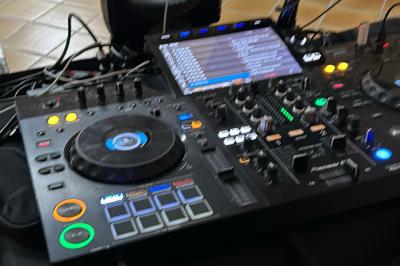 Table de mixage avec platines, microphones et panneau lumineux indiquant ’DJ Olivier’ sur une table en bois.