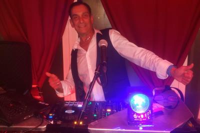 Table de mixage avec platines, microphones et panneau lumineux indiquant ’DJ Olivier’ sur une table en bois.