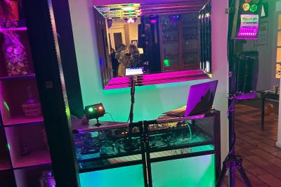 Table de mixage avec platines, microphones et panneau lumineux indiquant ’DJ Olivier’ sur une table en bois.