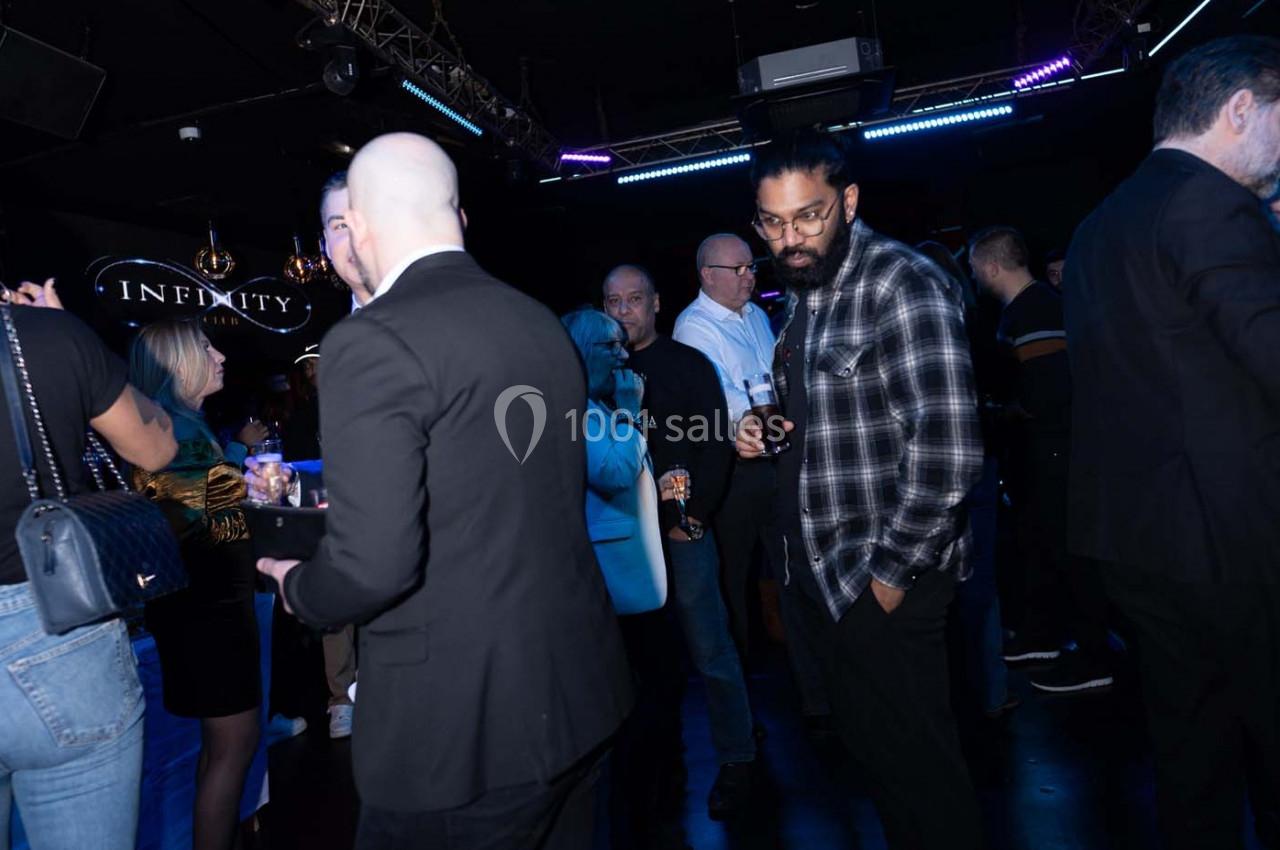 Des personnes discutent et socialisent dans un espace sombre éclairé par des lumières colorées.