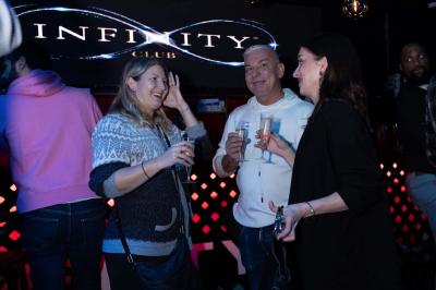 Entrée d'un club nocturne avec enseigne lumineuse ’Infinity Club’ et porte ornée de motifs décoratifs.