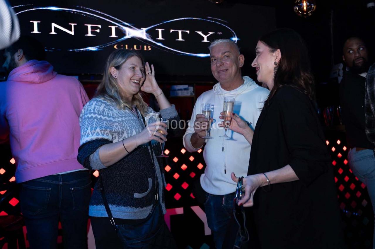 Des personnes discutent et rient en tenant des verres dans un club avec une enseigne lumineuse en arrière-plan.