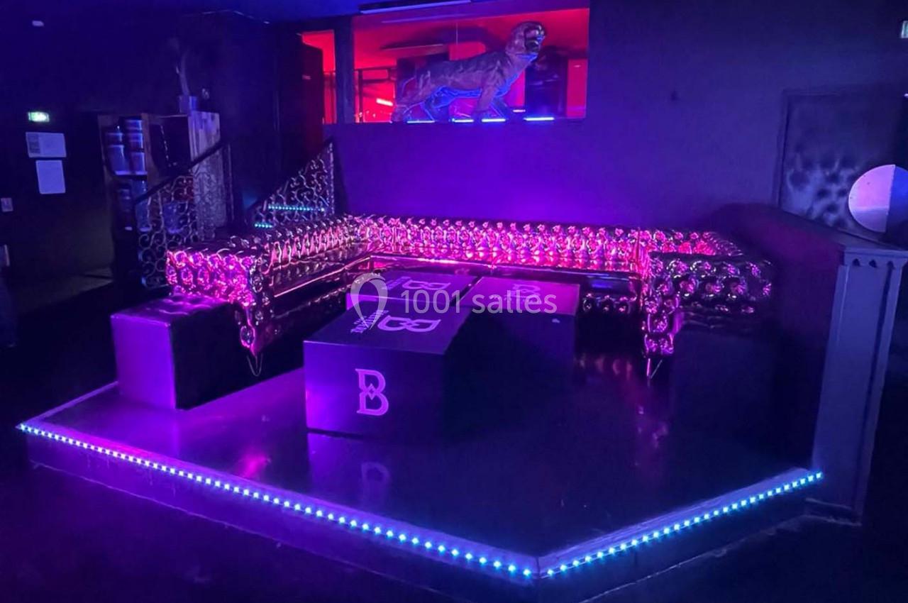 Canapé en cuir noir avec motifs lumineux, entouré de tables basses dans une ambiance tamisée aux lumières colorées.