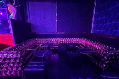 Entrée d'un club nocturne avec enseigne lumineuse ’Infinity Club’ et porte ornée de motifs décoratifs.