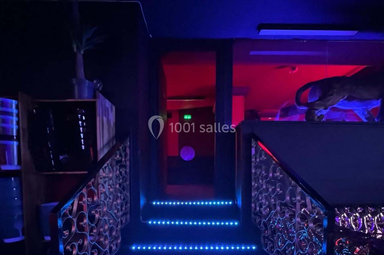 Escalier éclairé par des lumières LED bleues menant à une pièce sombre illuminée de rouge.