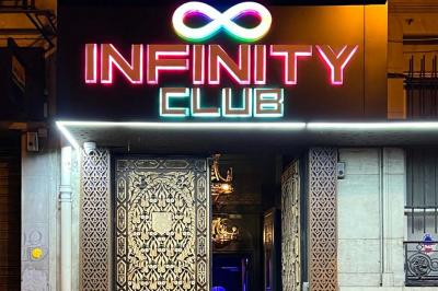 Entrée d'un club nocturne avec enseigne lumineuse ’Infinity Club’ et porte ornée de motifs décoratifs.