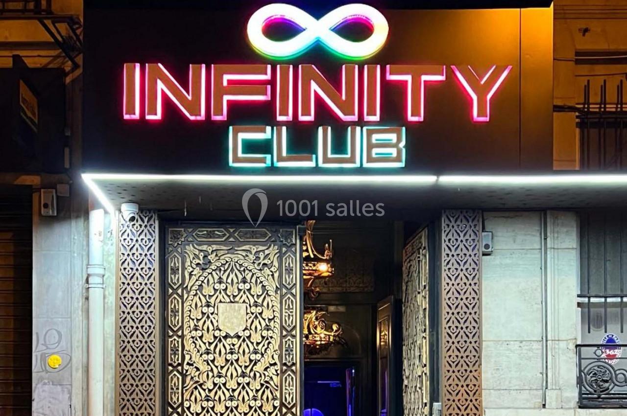 Entrée d'un club nocturne avec enseigne lumineuse ’Infinity Club’ et porte ornée de motifs décoratifs.