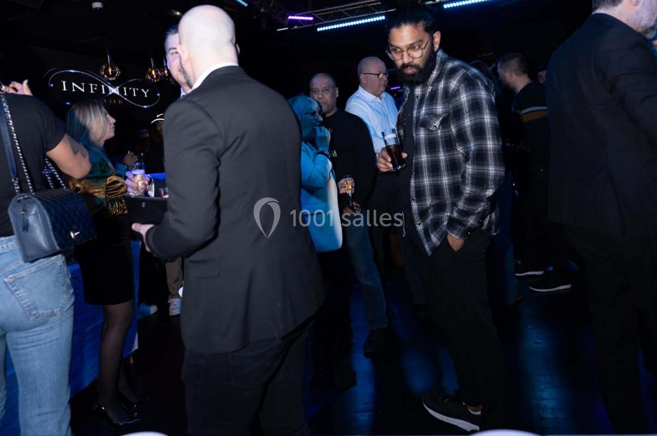 Personnes discutant et tenant des verres lors d'un événement social dans un espace sombre avec éclairage tamisé.