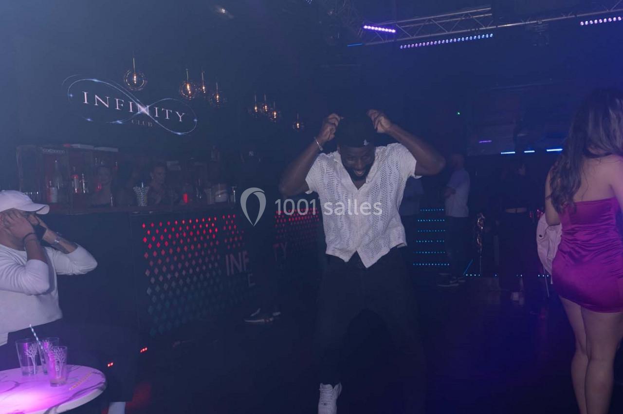 Un homme danse sur une piste de boîte de nuit, entouré de lumières colorées et de quelques personnes.