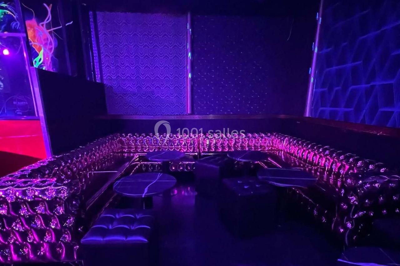 Banquette capitonnée violette entourant des tables basses dans un espace sombre à l'éclairage tamisé.