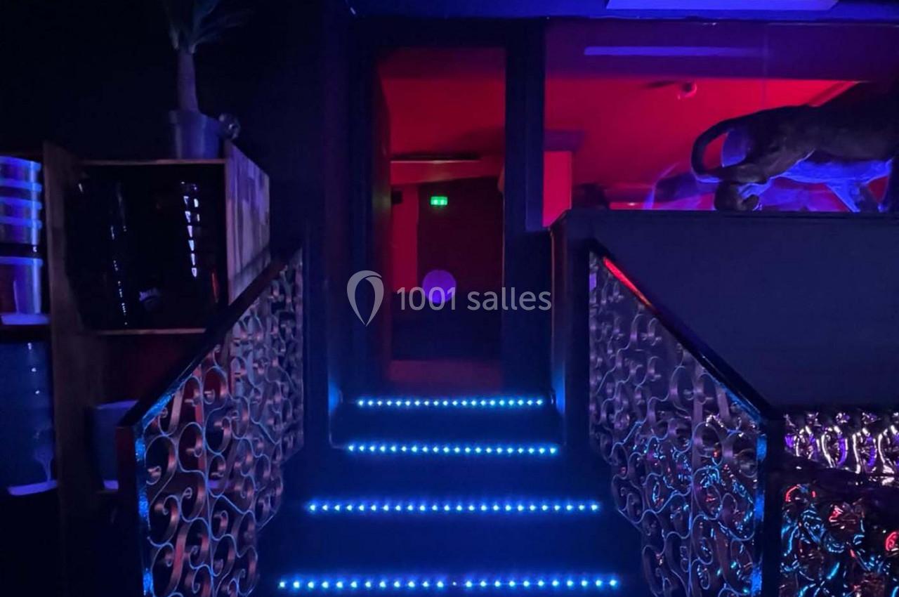 Escalier éclairé par des lumières LED bleues menant à une pièce sombre illuminée par une lumière rouge.