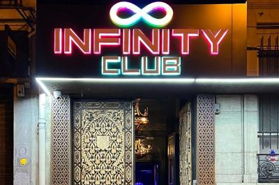 Façade d'un club nocturne avec enseigne lumineuse ’Infinity Club’ et porte ornée de motifs décoratifs.