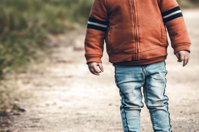 Un enfant souriant en t-shirt blanc pose avec une main sous le menton sur un fond clair.