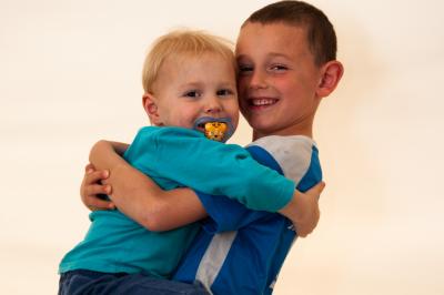Un enfant souriant en t-shirt blanc pose avec une main sous le menton sur un fond clair.