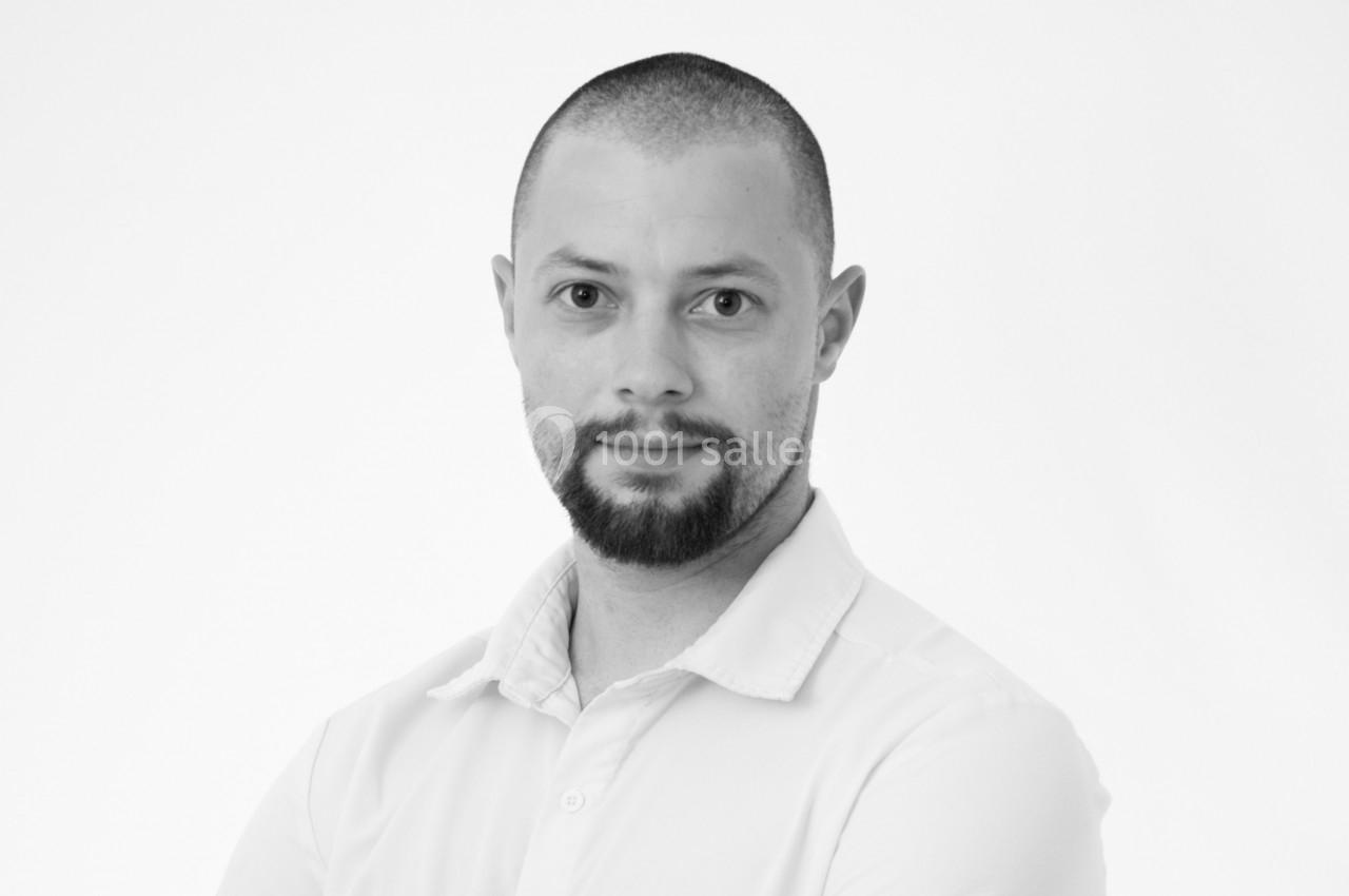 Portrait en noir et blanc d'un homme au crâne rasé et barbe, portant une chemise claire, regardant vers l'objectif.